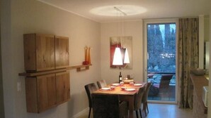A dining area with a wooden cabinet, a table set for four, and a view of the outdoors through a glass door. - Exklusives Apartment, am Luganersee, mit Außenpool by Interhome (MAROGGIA)