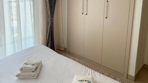 Hotellihuone, jossa on sänky, kaksi pyyhettä, vaatekaappi ja läpikuultavat verhot.