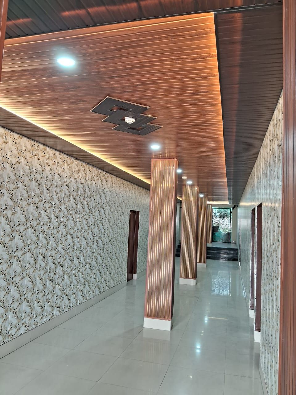 A modern hallway with patterned walls, wooden columns, and recessed lighting.