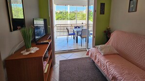 Una habitación con sofá, televisor, mueble de madera y balcón con mesa y sillas.
