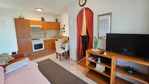 Un espacio habitable compacto con kitchenette, zona de comedor y área de estar con televisión.