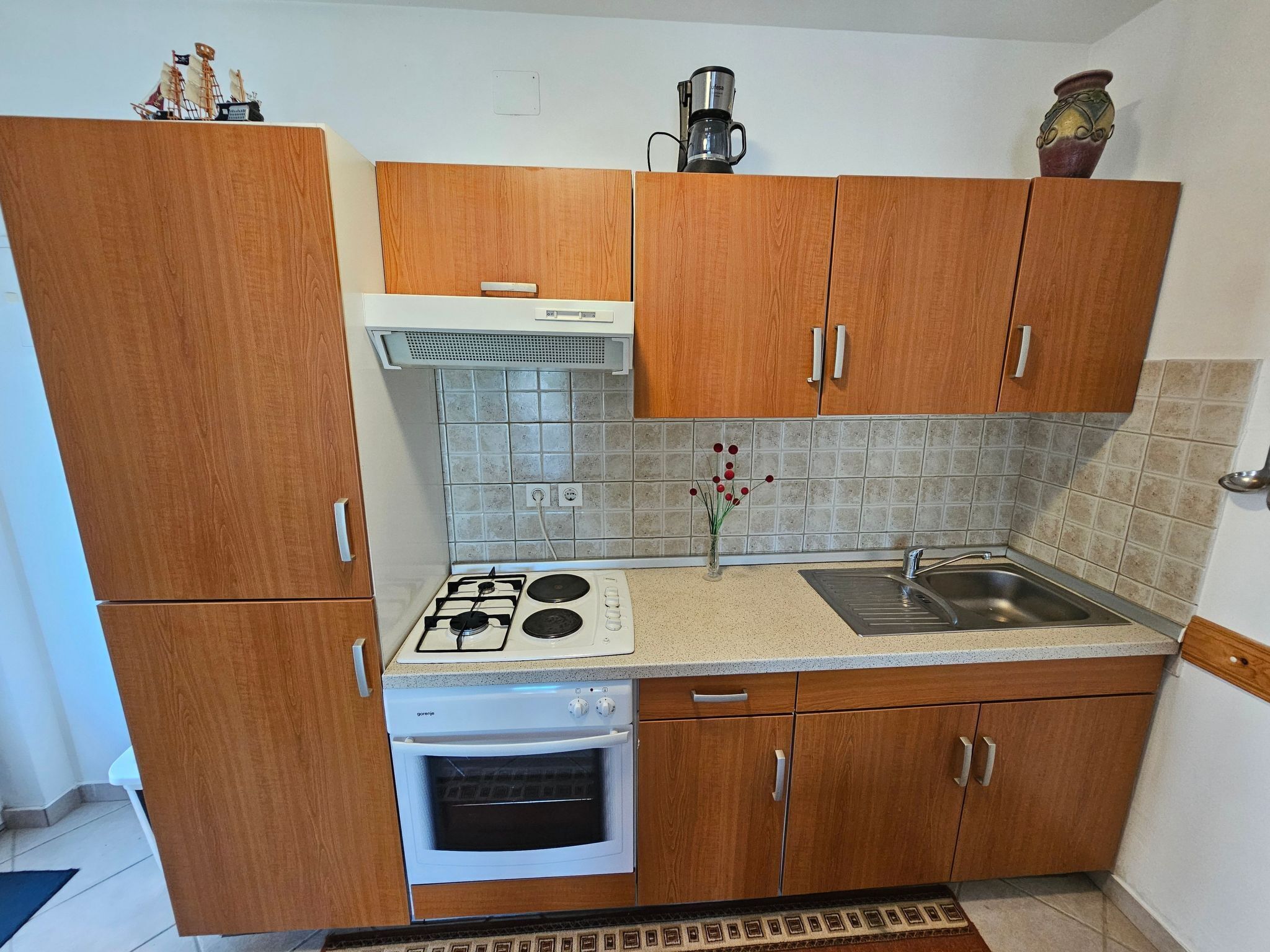 Una cocina compacta con armarios de madera, estufa a gas, horno, lavabo y cafetera sobre la encimera.