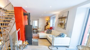 Een moderne woonkamer met een witte bank, een zwarte haard en een trap met een rode accentmuur.