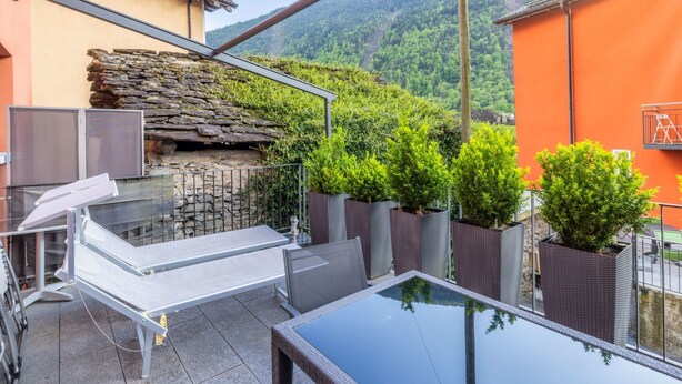 Een terras met een glazen tafel, een stenen muur en planten in potten.