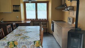 A compact kitchen with a dining table, chairs, a stove, and a window with blinds. - 'Cà da Rör' mit Bergblick by Interhome (Acquarossa)
