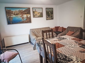A room with a bed, a sofa, a dining table, and three paintings on the wall.