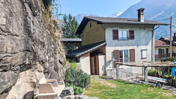 A stone bench, a stone table, and a stone fireplace in a courtyard with a mountain backdrop. - 'Cà da Rör' mit Bergblick by Interhome (Acquarossa)