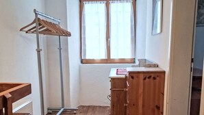 A room with wooden flooring, a wooden wardrobe, a metal drying rack, and a window with curtains. - 'Cà da Rör' mit Bergblick by Interhome (Acquarossa)