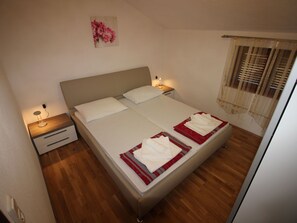 A neatly made bed with white linens and red accents, a bedside table with a lamp, and a wall-mounted painting. - "Manda3" mit Blick auf das Wasser by Interhome (Novi Vinodolski)