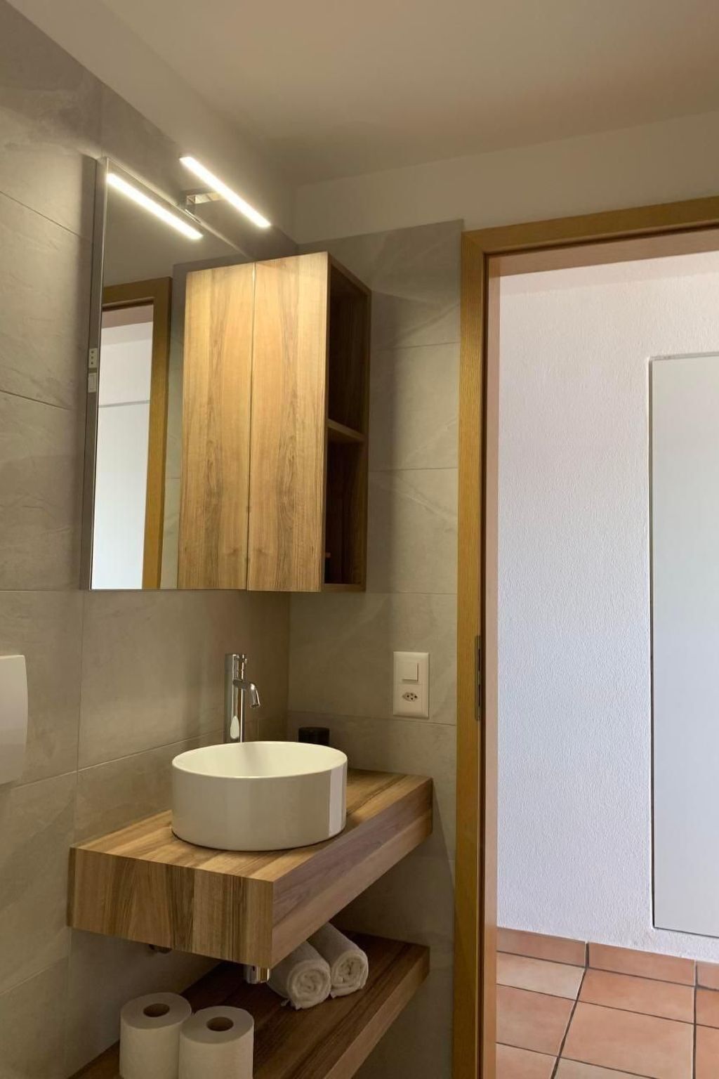 A bathroom with a wooden vanity, a round sink, and a mirror above it.