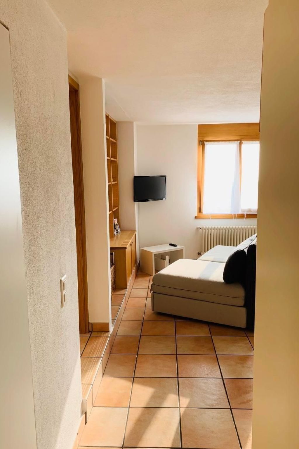 Une chambre à coucher avec un lit, un téléviseur fixé au mur, une fenêtre avec des stores et un radiateur.