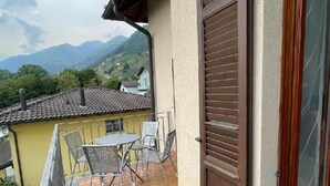 A balcony with a table and chairs, a closed wooden door, and a view of mountains in the background. - mit Bergblick by Interhome (Gordola)