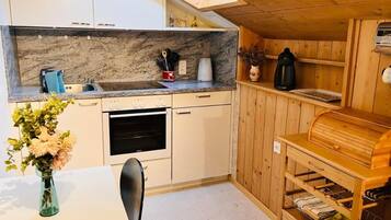Eine kleine Küche mit weißen Schränken, einem Einbauofen, einem Spülbecken und einem Holzregal mit einer Brokkiste.