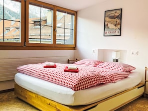 A hotel room with a bed, a window, a poster on the wall, and a view of buildings outside.