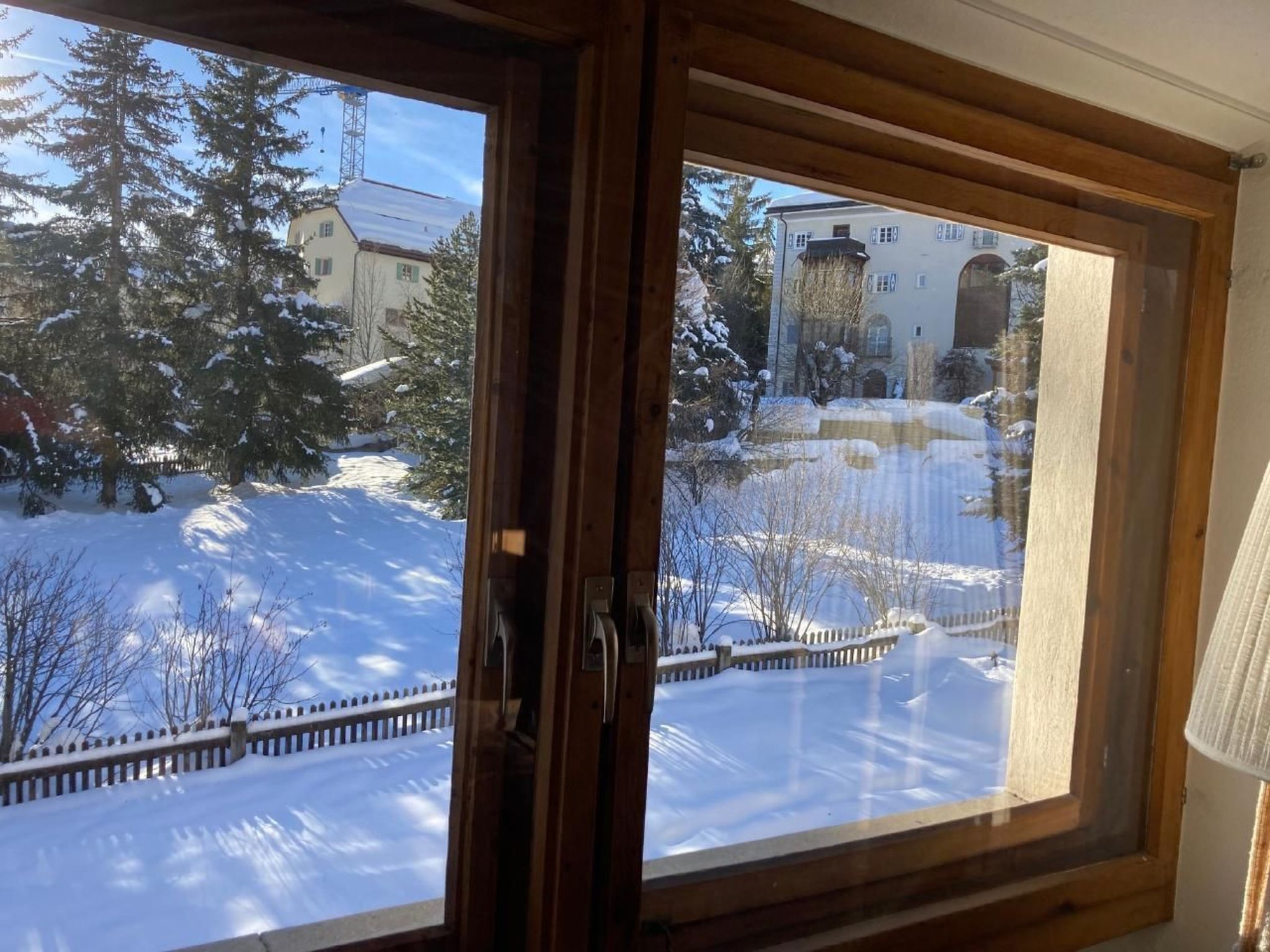 Ein Fenster mit Blick auf eine verschneite Landschaft, einschließlich Bäumen und Gebäuden.