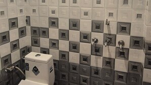 Une salle de bain avec des murs et un sol recouverts de carreaux disposés en motif à carreaux, des toilettes et un espace douche.