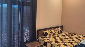 Une chambre à coucher avec un lit, un ventilateur de plafond, une fenêtre avec des rideaux, une petite table et un sol carrelé.