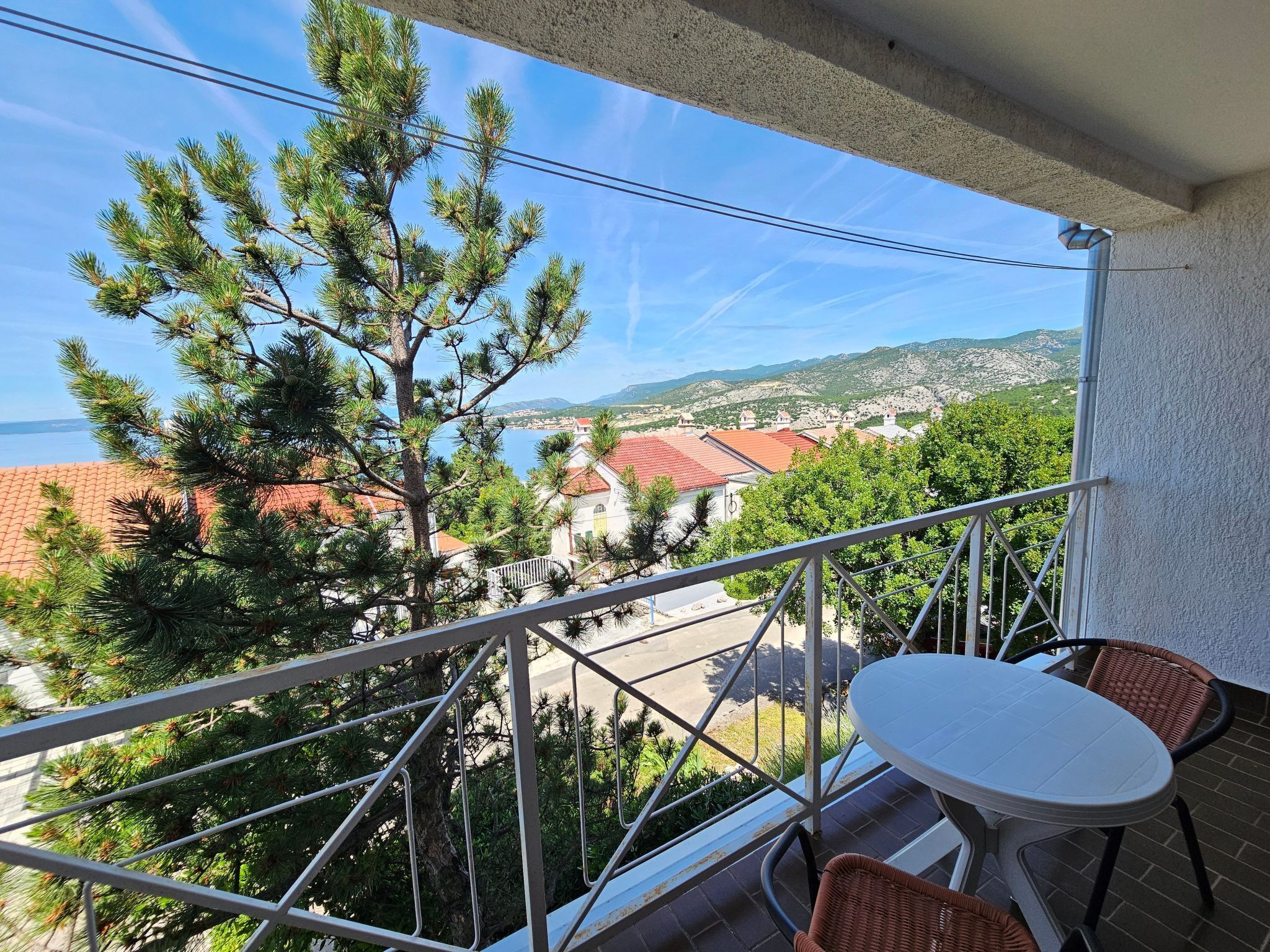 Un balcone con vista su una cittadina costiera, un tavolo e due sedie in vimini.