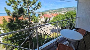 A balcony with a view of a coastal town, a table, and two wicker chairs. - für 6 Personen in Klenovica by Interhome (Novi Vinodolski/Klenovica)