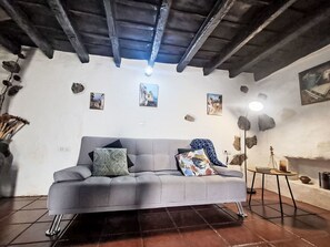A living room with a grey sofa, decorative pillows, a small table, and a stone wall with pictures. - Vacation home Trina by Interhome (Igueste)