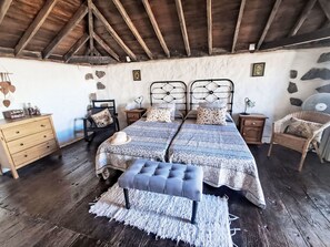 A rustic bedroom with two beds, a wooden dresser, a bench, and a stone wall. - Vacation home Trina by Interhome (Igueste)