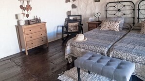 Un dormitori amb un taulell de fusta, una cadira, un llit amb roba de llit estampada, una panxa i un sostre rústic.