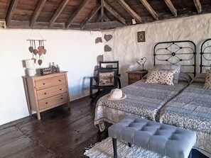 A bedroom with a wooden dresser, a chair, a bed with patterned bedding, a bench, and a rustic ceiling. - Vacation home Trina by Interhome (Igueste)