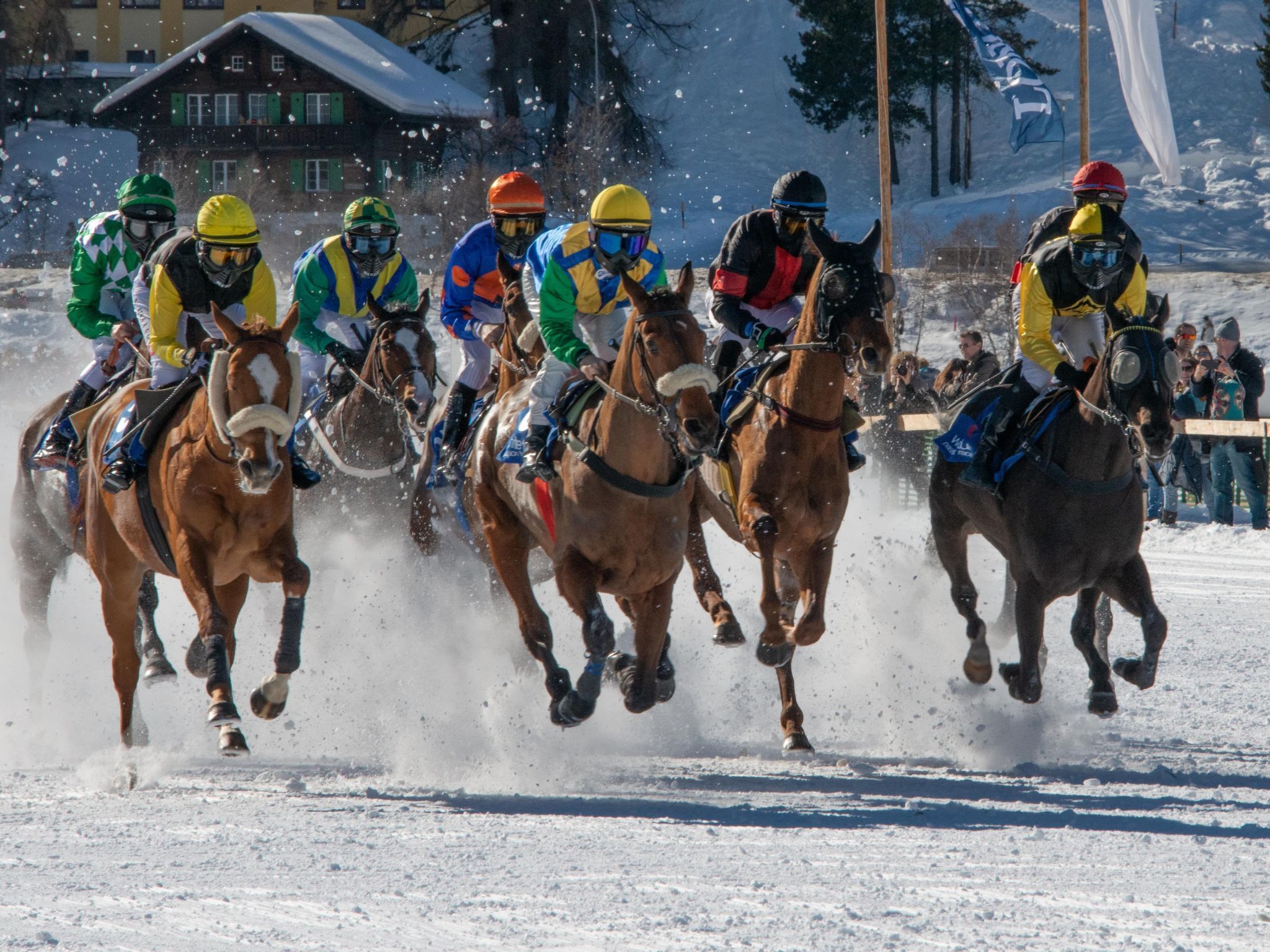 A group of horse riders in a race, with spectators in the background.