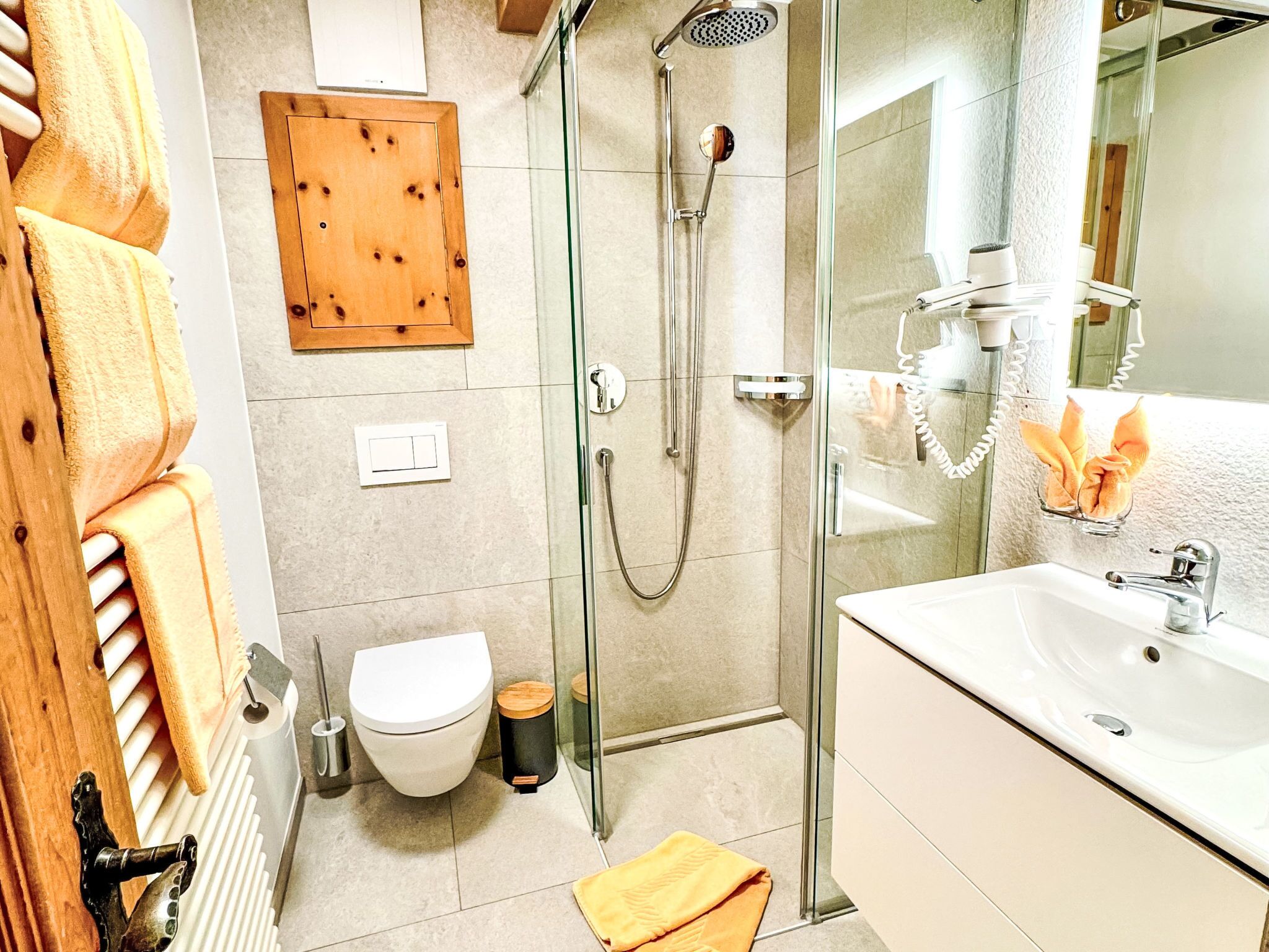 Un baño moderno con cabina de ducha de vidrio, un lavabo blanco y un perchero de madera.