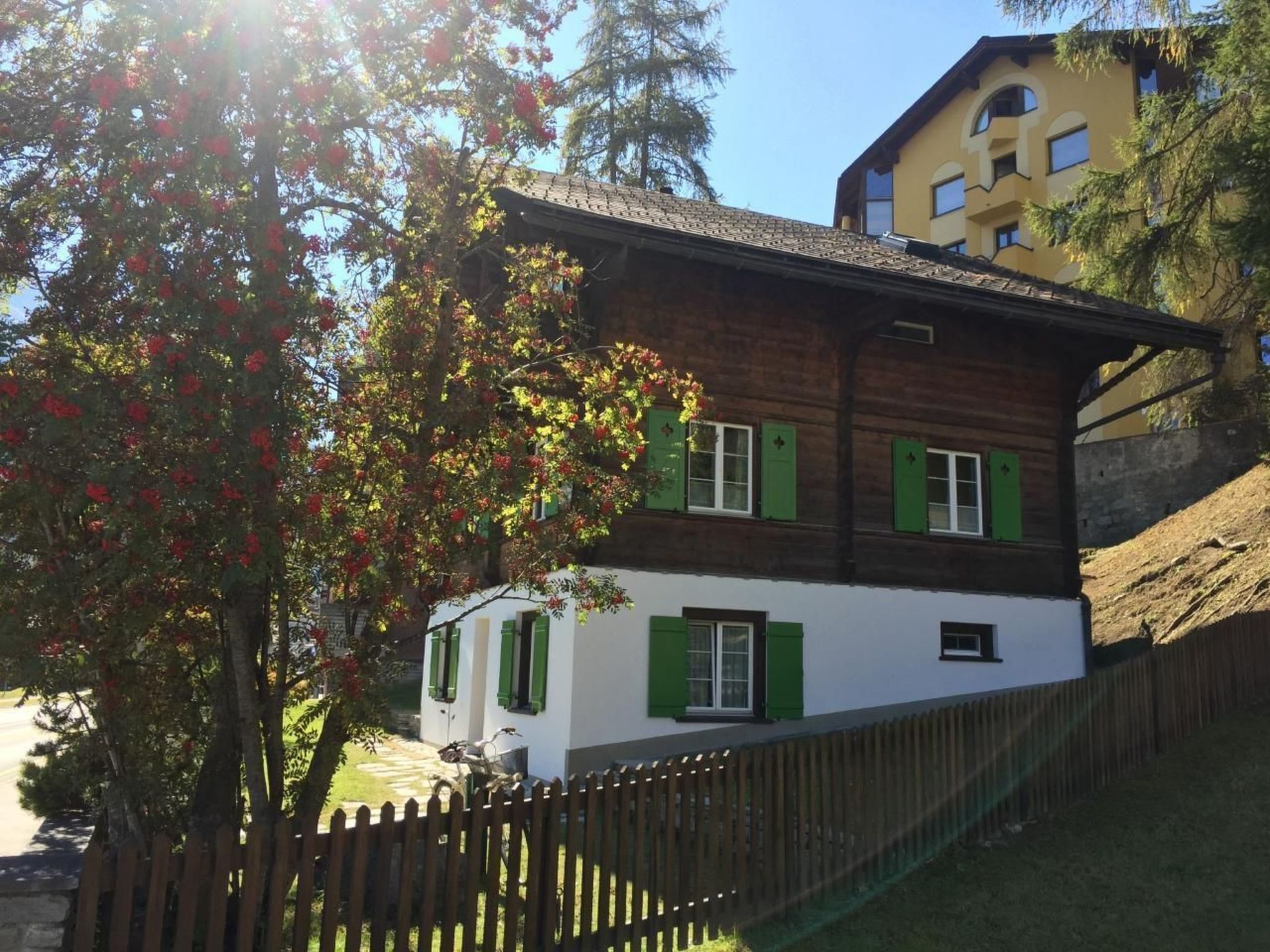 A two-story house with green shutters and a wooden fence.