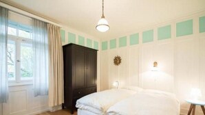 Ein Schlafzimmer mit Bett, Kleiderschrank, einem Fenster mit Vorhängen und einer Wandleuchte.