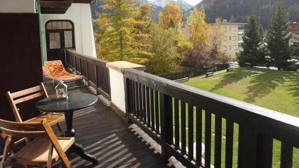 Ein Balkon mit Holzgeländern, einem Tisch und zwei Stühlen.