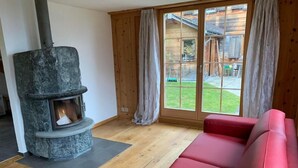 Ein gemütliches Wohnzimmer mit Kamin aus Stein, einem roten Sofa und großen Fenstern mit Vorhängen.