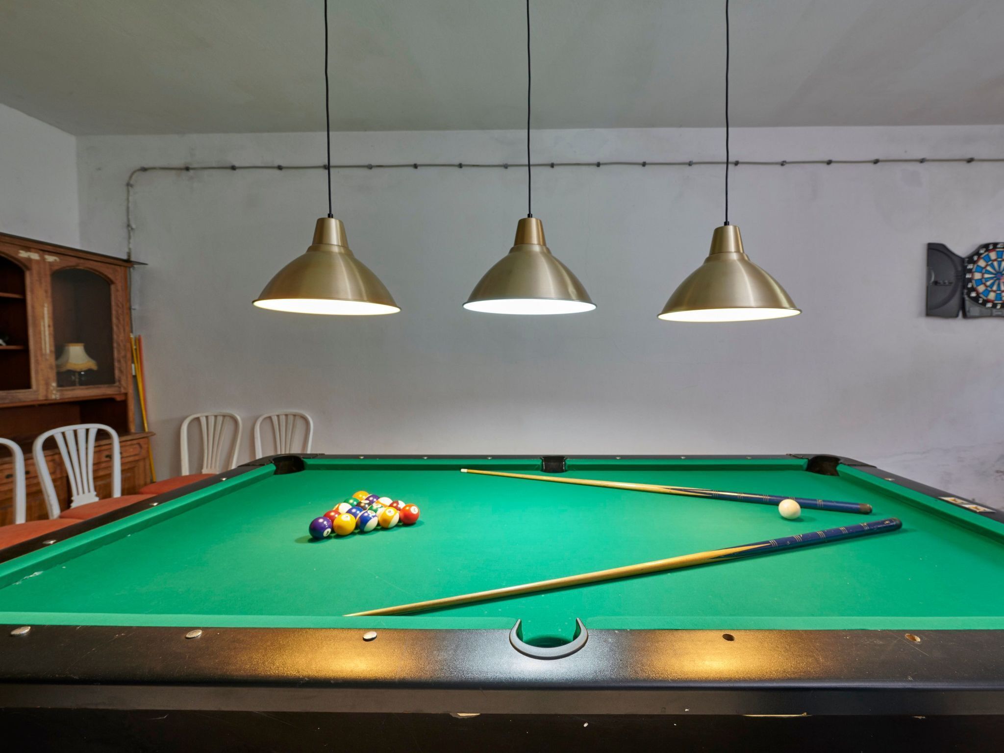 Une table de billard avec trois lampes suspendues, un queue de billard et un jeu de billes.