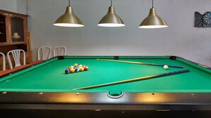 Ein Billardtisch mit drei Hängelampen, einem Schläger und einem Satz Billardkugeln.