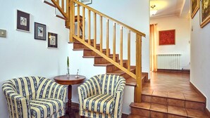 Eine Treppe mit Holzwertlauf und Fliesenboden. Zwei gepolsterte Stühle mit Streifenmuster und ein kleiner runder Tisch mit einer Vase.