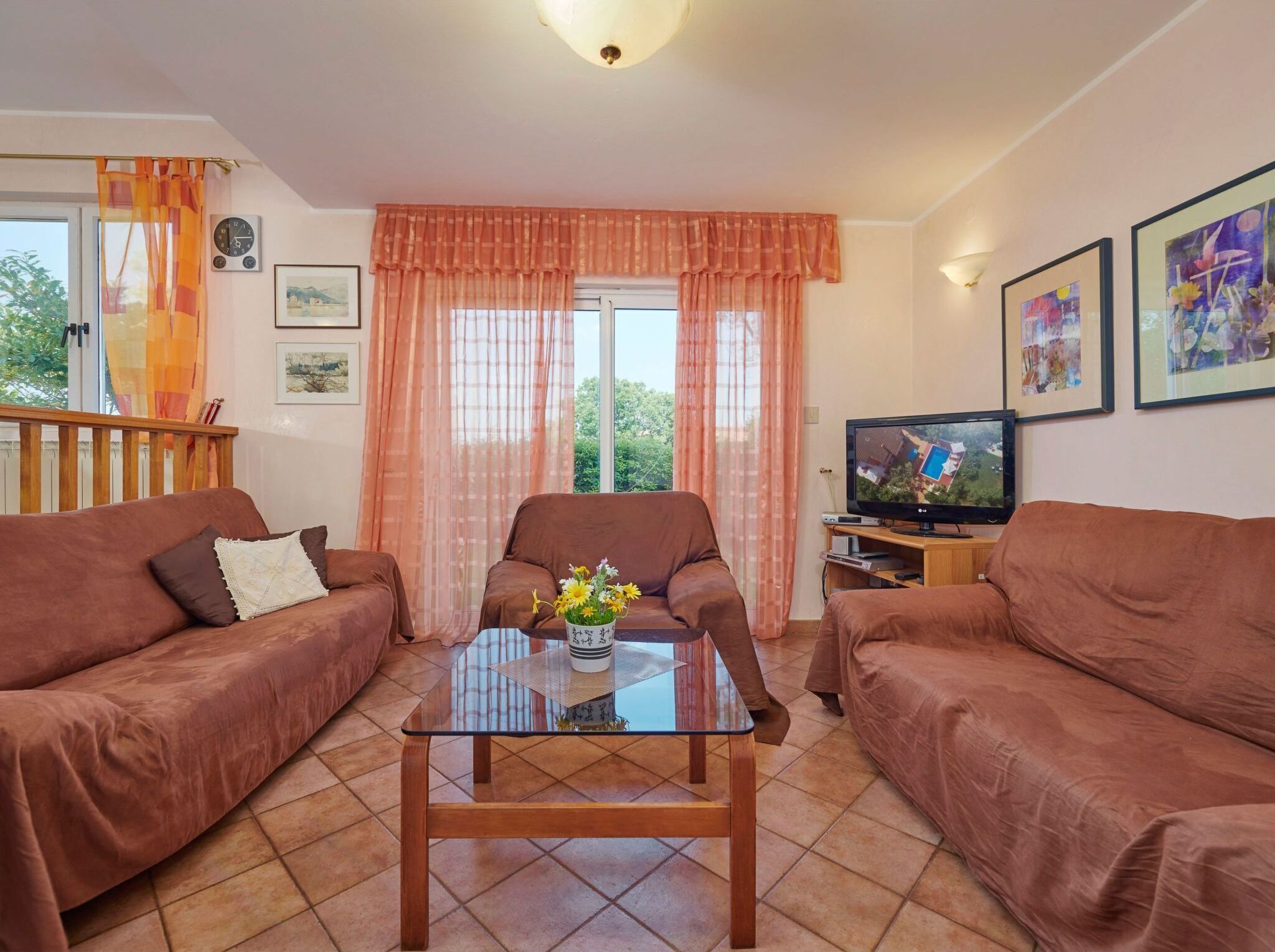 A living room with two brown sofas, a glass coffee table with a vase, a television, and framed pictures on the wall.