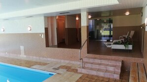 Ett inomhusområde med en pool där man tydligt kan se poolen, en trappa som leder upp till en sittgrupp och en glasvägg som avgränsar poolen från sittgruppen.