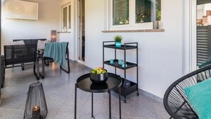 A modern outdoor seating area with a black metal table, a black metal chair, and a black metal shelf with a plant and decorative items. - Wohnung mit Blick auf das Wasser by Interhome (Pula)