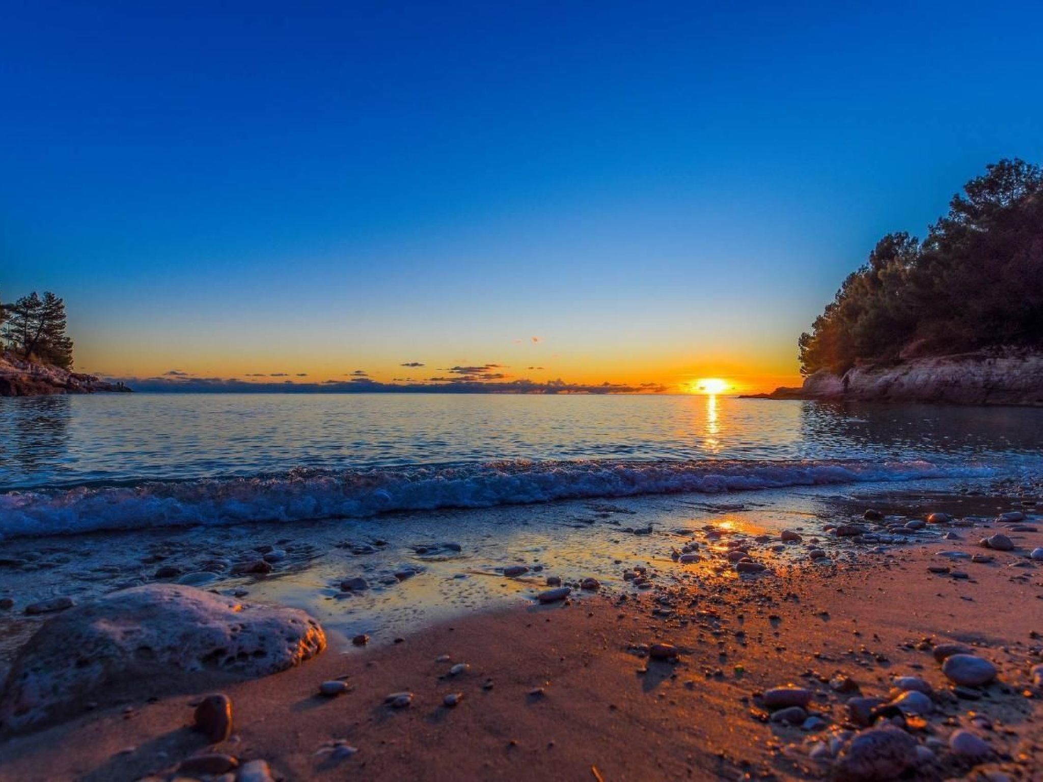 Une plage au coucher du soleil, avec une eau calme et des rochers éparpillés.