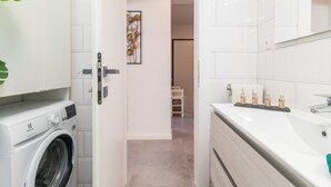 A modern bathroom with a washing machine, a sink with toiletries, and a hallway leading to another room. - Wohnung mit Blick auf das Wasser by Interhome (Pula)