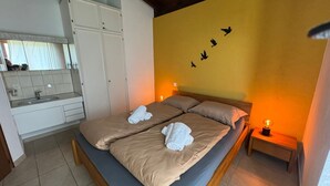 A bedroom with a bed, two pillows, a nightstand with a lamp, a bathroom with a sink and mirror, and a wall with bird decals. - Casa Rena by Interhome (Ascona)