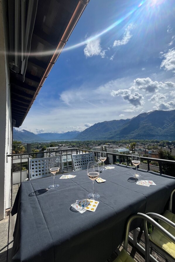 A table set with wine glasses and playing cards on a balcony overlooking a mountainous landscape.