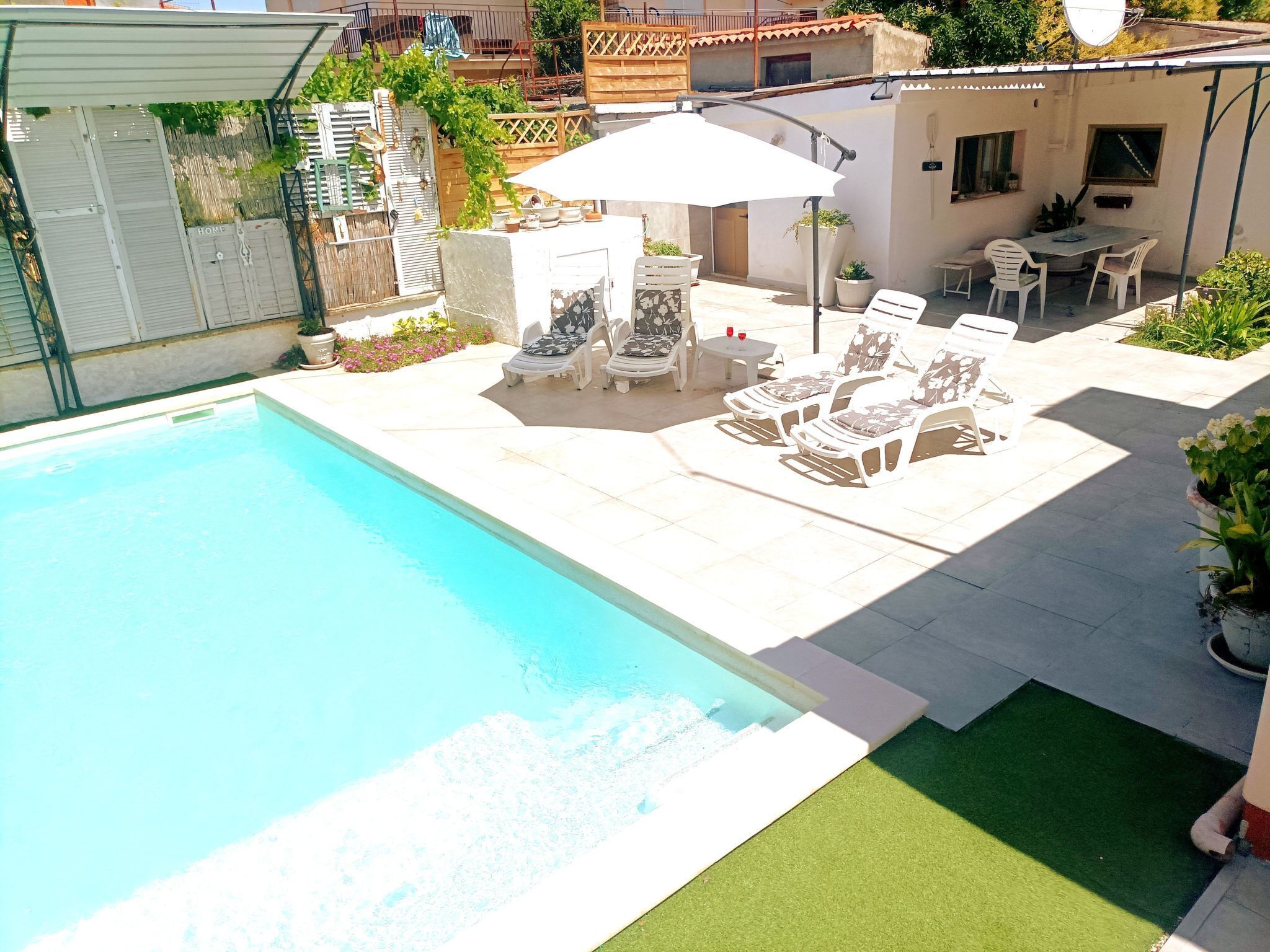 Una piscina con lettini e un tavolo, circondata da un patio con piante e un piccolo edificio.