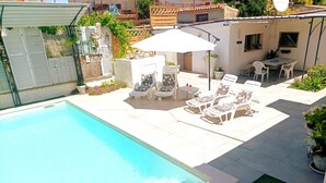 A swimming pool with lounge chairs and a table, surrounded by a patio area with plants and a small building. - Haus in Pula mit privatem Pool by Interhome (Pula)