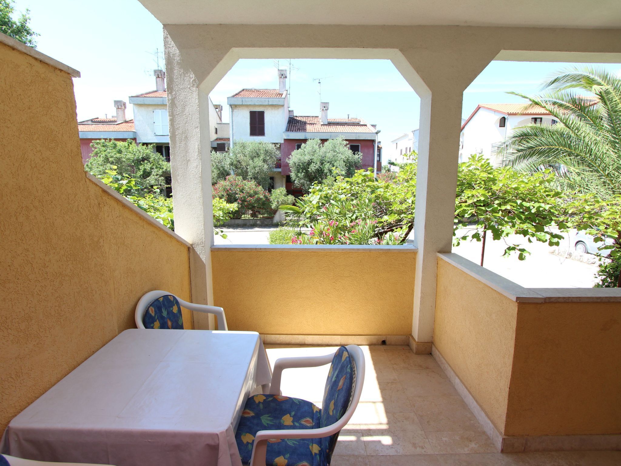 Ein Balkon mit Tisch und Stühlen, der auf einen Wohnbereich mit Häusern und Grünflächen blickt.