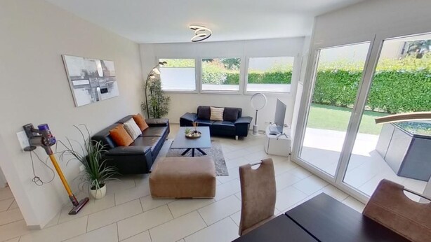 Ein geräumiges Wohnzimmer mit Sofa, Couchtisch und Essbereich mit Tisch und Stühlen. Ein großes Fenster bietet Blick ins Freie.
