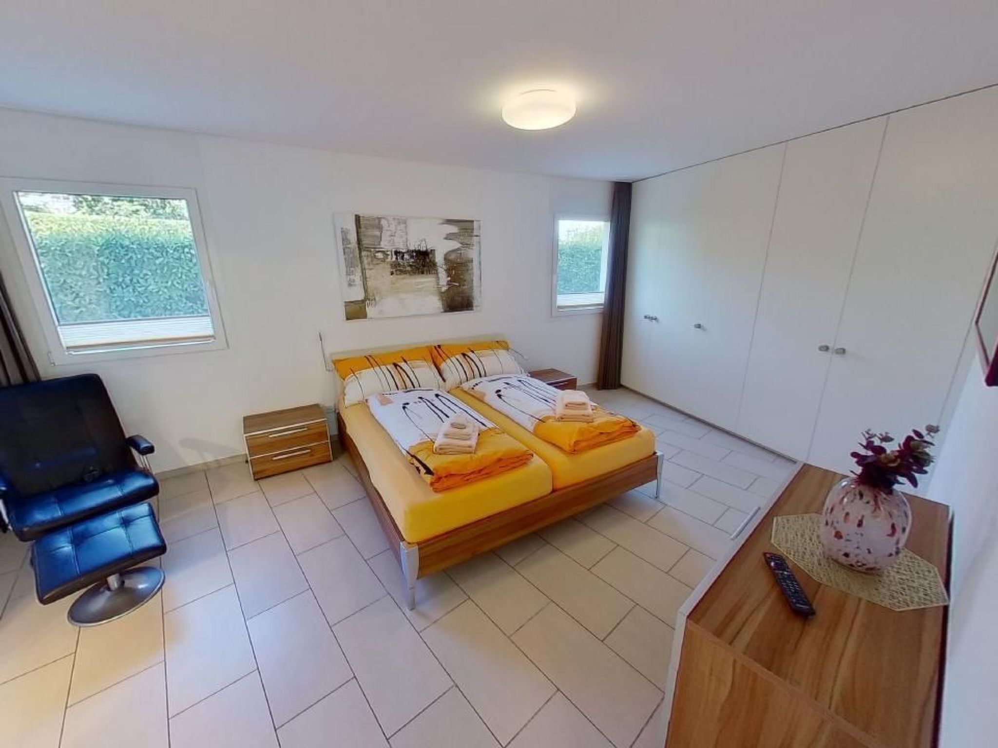 Une chambre à coucher avec un lit, une chaise, un bureau orné d’un vase et un tableau accroché au mur.