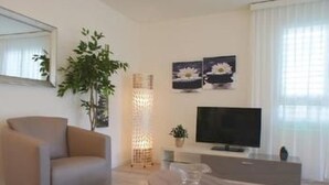 A modern living room with a sofa, a TV, a plant, and artwork on the wall. - Residenza San Materno Apt. 3 by Interhome (Ascona)