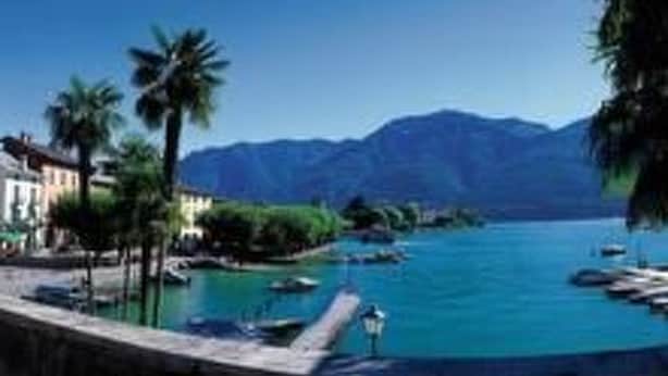 A coastal town with a marina, buildings, and mountains in the background. - Residenza San Materno Apt. 3 by Interhome (Ascona)